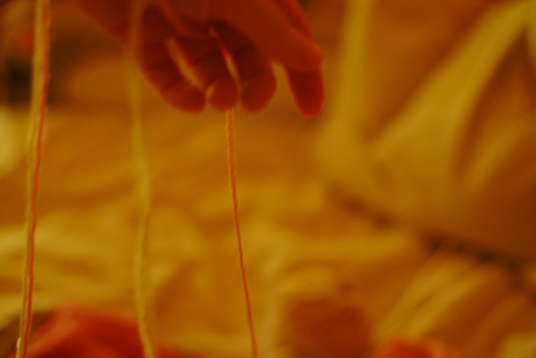 A hand holding orange and yellow yarn in warm light